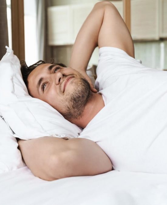 Smiling young man laying on a pillow in bed